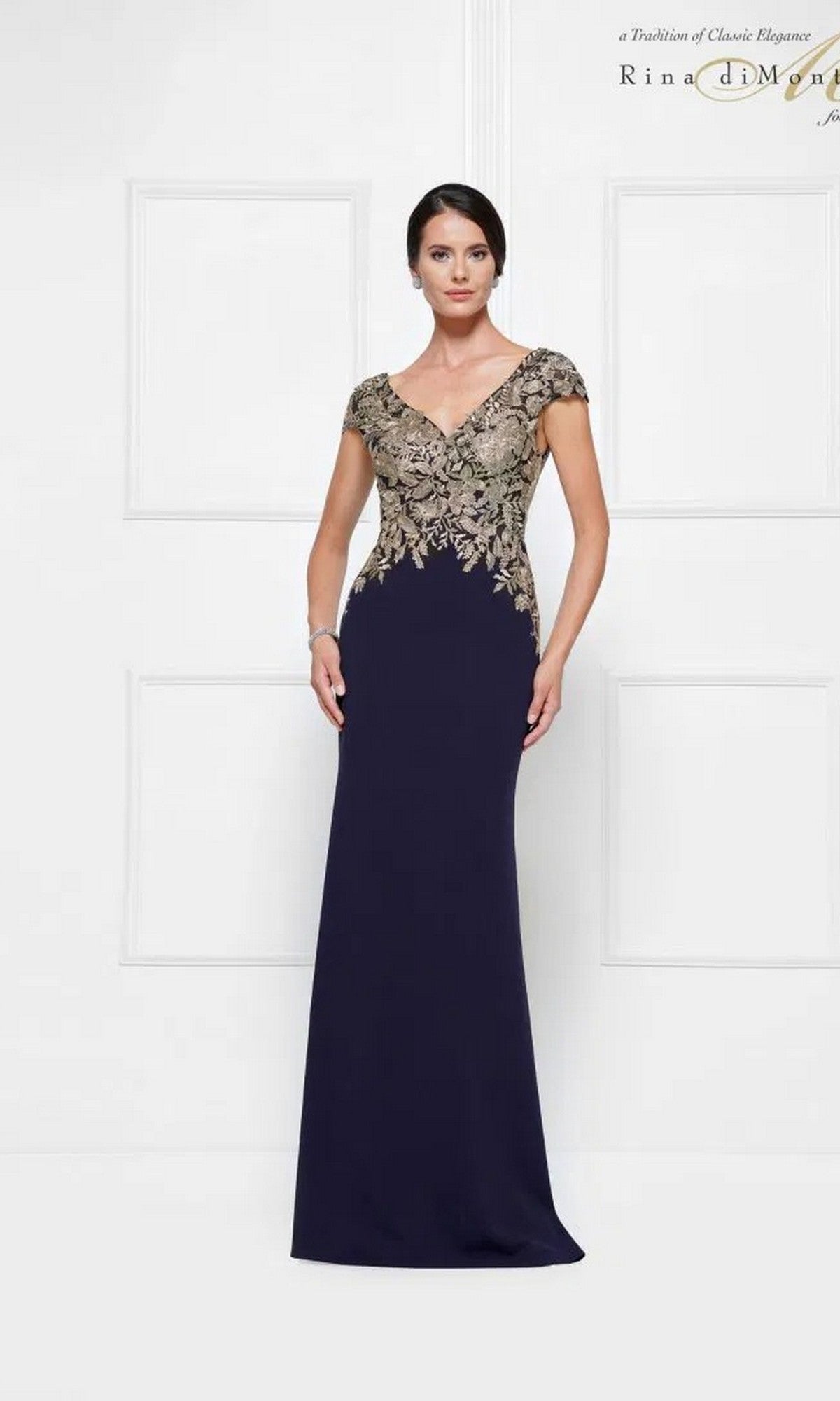 Woman in the Long Formal Dress: Rina Di Montella RD2652, featuring a floor-length navy & gold sheath design with fitted, gold-embroidered bodice and cap sleeves, standing against a plain white background.